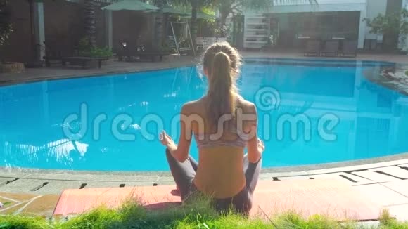 女孩坐在瑜伽姿势莲花在游泳池的背面视频的预览图