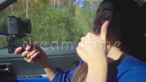 一位年轻的黑发女子坐在车里用相机为她的频道拍摄视频视频的预览图