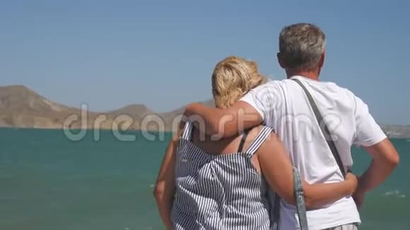 成熟的情侣拥抱俯瞰大海一对漂亮的老人在水边在户外牵手的老人视频的预览图