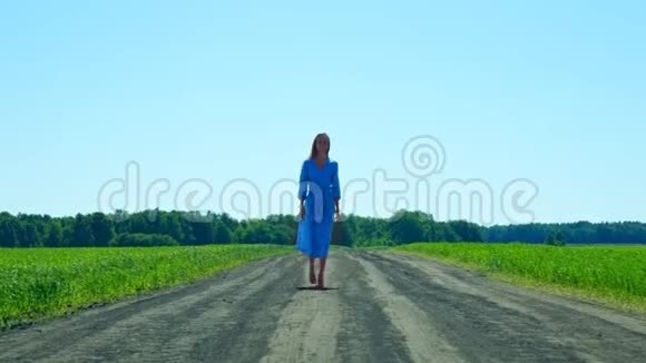 一位身穿蓝色长裙的妇女在田野边的路上走近视频的预览图