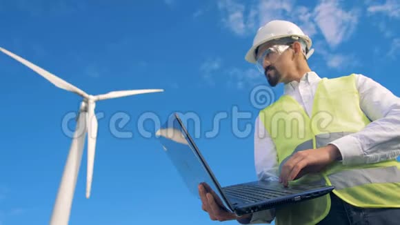 男性工程师在他的笔记本电脑上打字站在电动风力涡轮机附近4K视频的预览图
