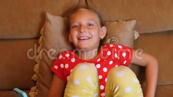快乐的少女微笑着在家庭舒适的沙发上使用智能手机视频的预览图