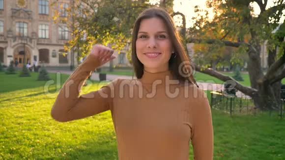 快乐的白种人黑发女孩的肖像使手指向上显示喜欢和尊重绿色公园的背景视频的预览图