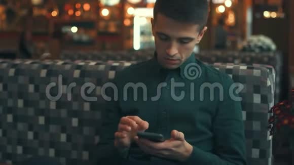 帅哥环顾四周用他的智能手机坐在咖啡馆里聊天时髦的样子俏皮的心情视频的预览图