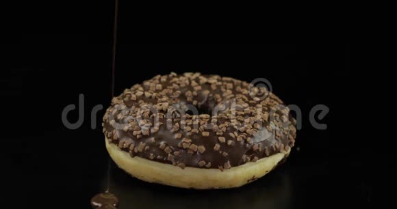 美味的融化黑巧克力糖浆倒在黑色背景的甜甜圈上视频的预览图