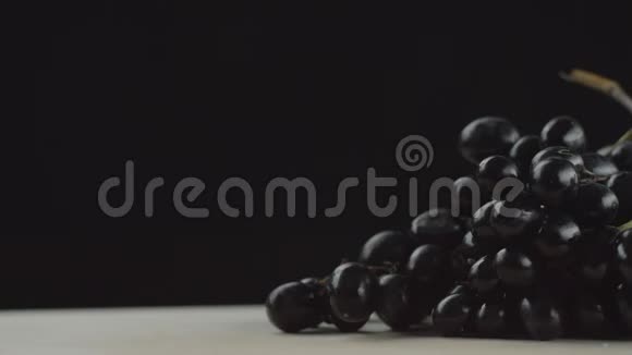 在视频中我们看到一串葡萄两颗葡萄从一串串的黑色背景在桌子上滚动视频的预览图