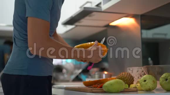 一名年轻人在厨房用新鲜的热带水果为家人准备早餐时慢镜头视频的预览图