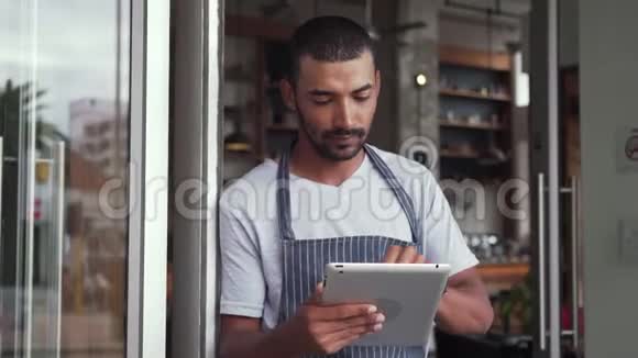 男主人站在他拿着数码平板电脑的咖啡馆门口视频的预览图