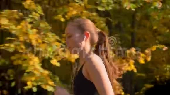 多莉拍摄的年轻迷人的白种人苗条女孩跑在秋季公园与电话和耳机视频的预览图