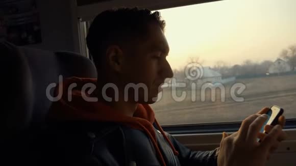 快乐年轻人在火车上使用智能手机坐在窗户对面美丽的日落视频的预览图