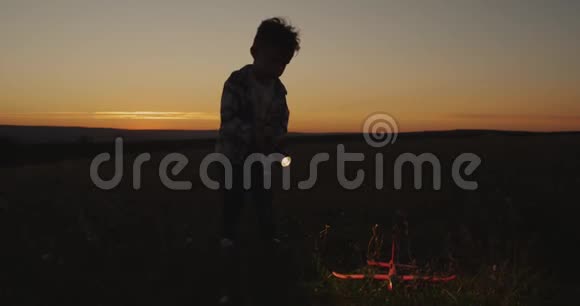 日落时分一个男孩在玩一个大手电筒和一架飞机穿过田野视频的预览图