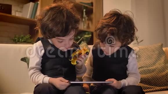 小阿拉伯卷头双胞胎坐在沙发上饶有兴致地看着客厅里的平板电脑视频的预览图
