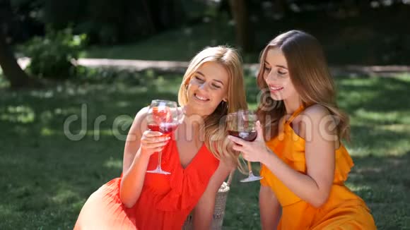 两个女孩穿着连衣裙坐在公园里喝酒视频的预览图