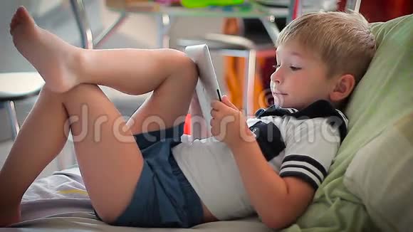 小男孩在床上躺在平板电脑上看故事视频的预览图