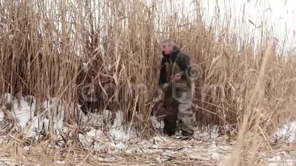 一个被雪覆盖的冰冻湖上的男性村民切断了干燥的芦苇了房子在烤箱里燃烧农村生活方式视频的预览图