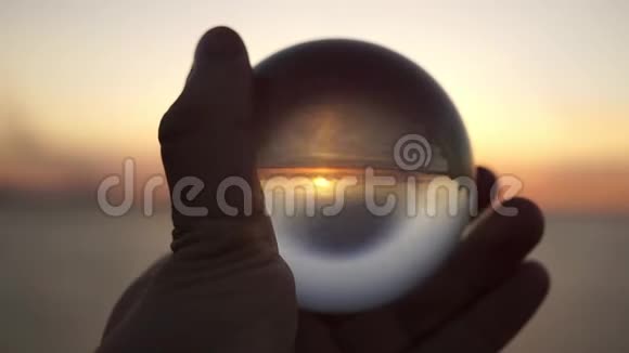 在海上日落的背景下雄手握着一个玻璃球戏剧性的电影镜头剪影视频的预览图