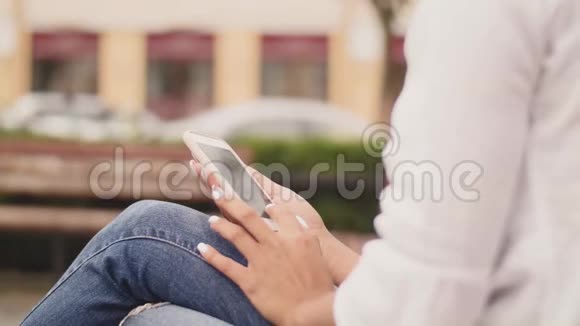 年轻女子在城市公园的长凳上用手机女孩手里拿着手机控制手指视频的预览图