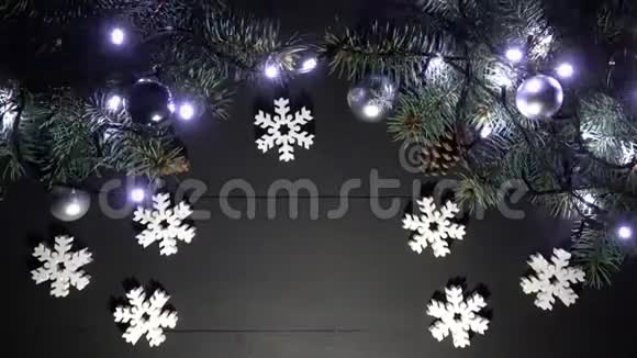 在黑色木桌上摆放着云杉树枝模糊的闪烁灯光圣诞球和雪花玩具的圣诞边框视频的预览图