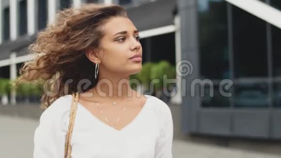 站在城市里的年轻女子的侧面肖像和风触摸她的头发视频的预览图