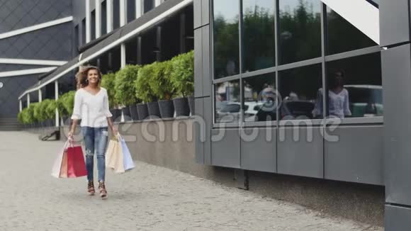 美丽微笑的女人走在街上漂亮的年轻女人带着购物袋快乐地走在市中心A视频的预览图