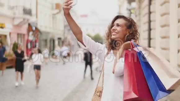 时尚快乐漂亮酷年轻女人带着购物袋在智能手机上做照片自画像视频的预览图