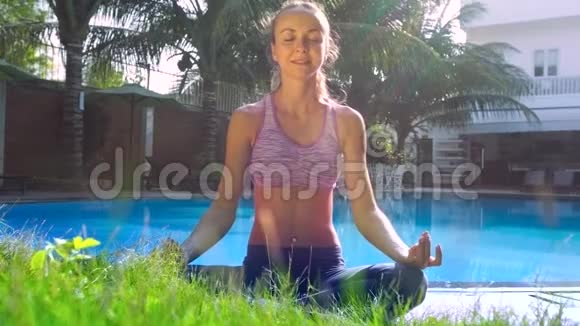 瑜珈中的女士在酒店的草地游泳池旁摆出莲花冥想的姿势视频的预览图