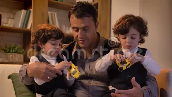 阿拉伯父亲坐在沙发上的肖像他的双胞胎儿子在客厅里玩玩具机器人视频的预览图