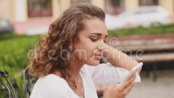 女人在长凳上用智能手机放松户外科技关门视频的预览图