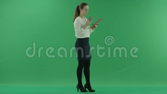一个年轻的女孩正在用手机说话在绿色屏幕上的剪贴板上写着一些东西视频的预览图