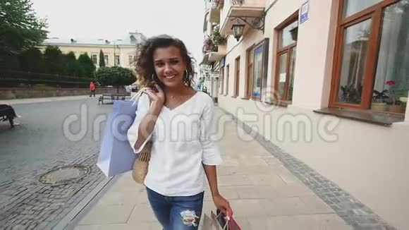 漂亮的年轻女人背着购物袋可爱的女孩购物后走在城市的街道上慢动作视频的预览图