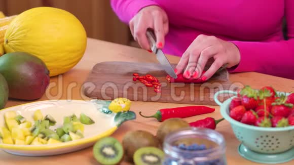 一个穿着粉色上衣的女人在桌子上切碎辣红辣椒视频的预览图