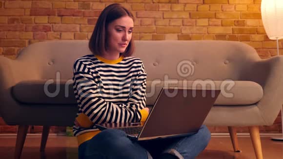 一张年轻漂亮女孩的特写照片她在笔记本电脑上打了一个视频电话在舒适的地板上开心地笑着视频的预览图