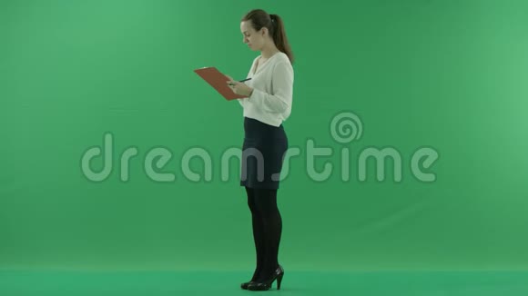 一个年轻的女孩正在用手机说话在绿色屏幕上的剪贴板上写着一些东西视频的预览图