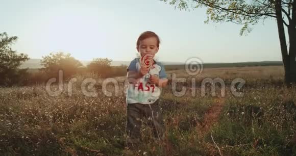 一岁的可爱男孩在大自然中吃棒棒糖非常有趣背景日落视频的预览图