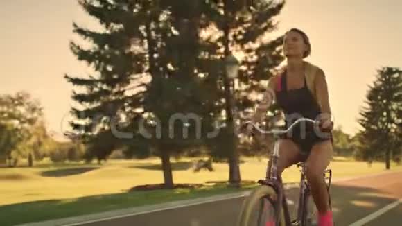 在金色夕阳下的夏日公园骑自行车的健身妇女视频的预览图