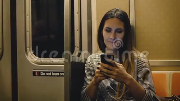 快乐轻松美丽的千禧女孩坐在地铁列车上在智能手机应用程序上在线观看视频微笑视频的预览图