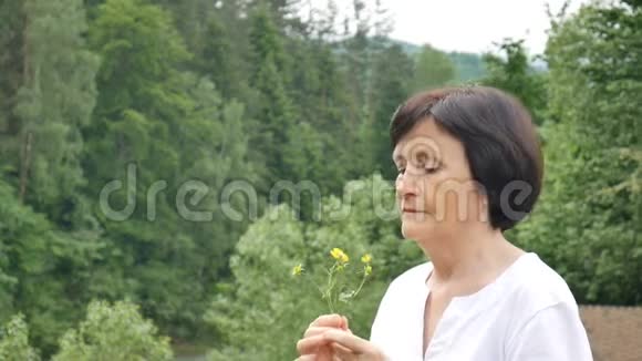 一位美丽的老年妇女在山林背景下的特写肖像手里拿着野花视频的预览图