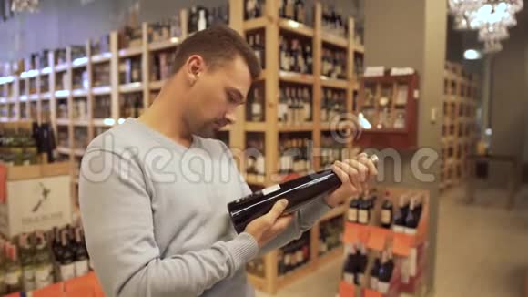 有魅力的家伙仔细检查了葡萄酒店里酒瓶标签上的成分酒瓶是视频的预览图