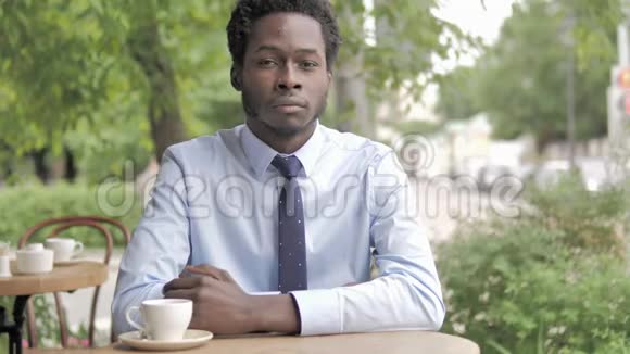 微笑的非洲商人坐在户外咖啡厅的肖像视频的预览图