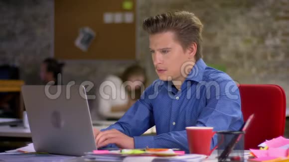 中年金发白种人商人在办公室里用笔记本电脑和喝咖啡的肖像视频的预览图