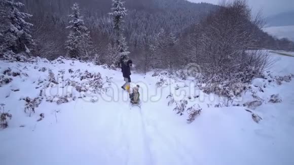 年轻的幸福家庭在雪林里玩得很开心父母把他们的小儿子卷在雪橇上晚上散步慢慢视频的预览图