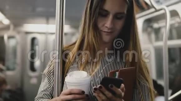 快乐成功的博客女孩在地铁列车上享受音乐智能手机应用程序耳机微笑咖啡杯视频的预览图