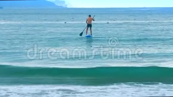 海浪翻滚海滩上的家伙在开阔的海洋上划桨板视频的预览图