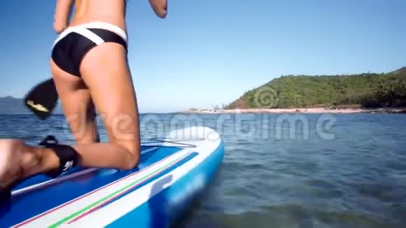 穿比基尼的金发女孩在绿色海岸划桨视频的预览图