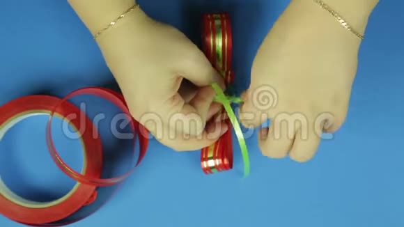 女人双手用绿色辫子绑起一个空白的红色丝带蝴蝶结蓝色背景视频的预览图