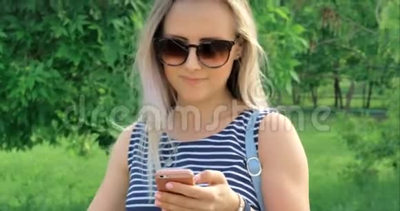 快乐的年轻妈妈带着眼镜在手机上输入短信和一个小孩子在街上散步视频的预览图