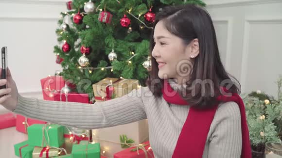 快乐快乐的年轻亚洲女人用智能手机自拍圣诞树装饰她的客厅在家圣诞节视频的预览图