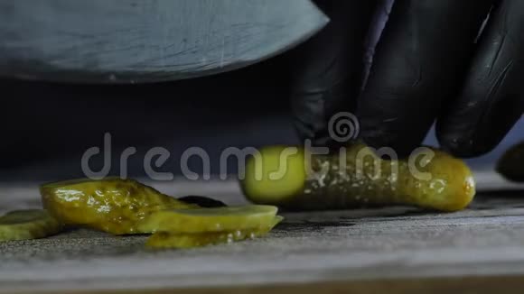 这位厨师正在剪一根咸黄瓜这根黄瓜被放在一块木板上上面是一块孤立的黑色背景视频的预览图