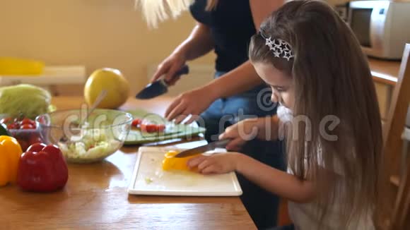 妈妈教她的小女儿切沙拉女孩在厨房里切黄椒妈妈助理视频的预览图