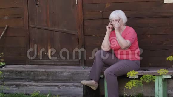 坐在家门口的老妇人在乡下打手机视频的预览图